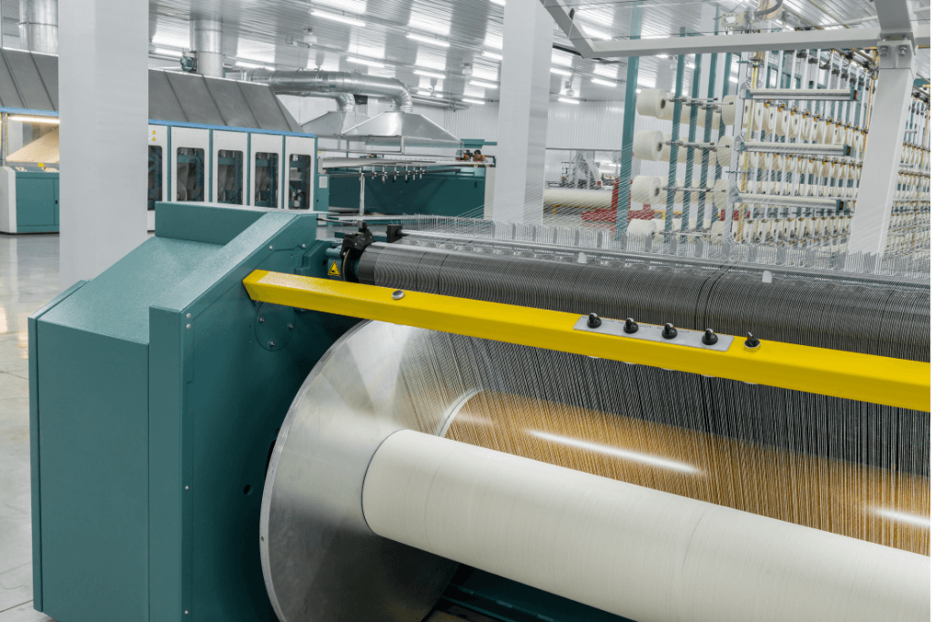 Máy dệt công nghiệp hiện đại trong nhà máy, đang vận hành các cuộn sợi lớn để dệt vải; minh họa cho thành phần và quy trình sản xuất vải.